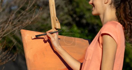 Woman painting abstract art on a canvas outdoors with peach-colored paint