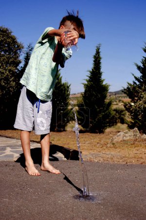 Téléchargez les photos : Enfant jetant de l'eau d'un verre sur le sol - en image libre de droit