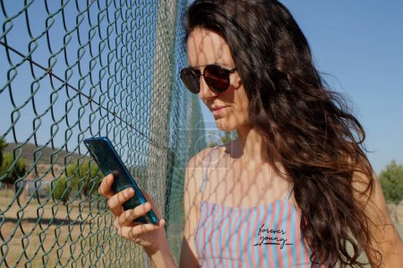 Frau mit langen Haaren und Sonnenbrille mit Handy auf dem Land