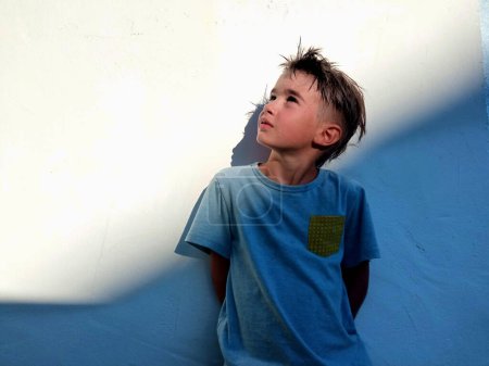 Kind steht an eine weiße Wand gelehnt mit Licht und Schatten, die nach oben schauen