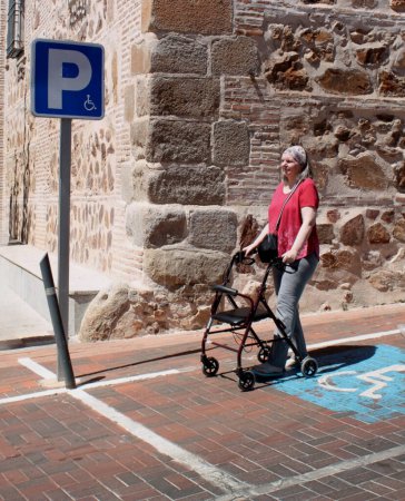 Woman with reduced mobility walking with a walker and a parking sign for people with reduced mobility