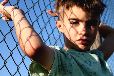 Boy looking at camera attached to a fence