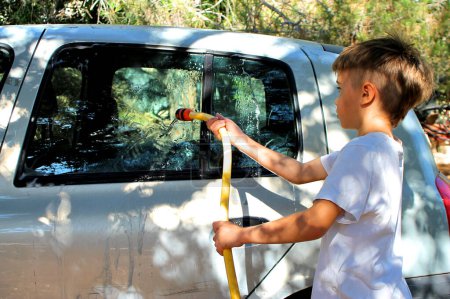 Téléchargez les photos : Child cleaning a car with a hose - en image libre de droit