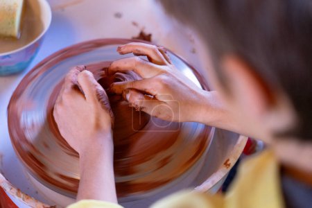 Boy learning to make pottery on the wheel