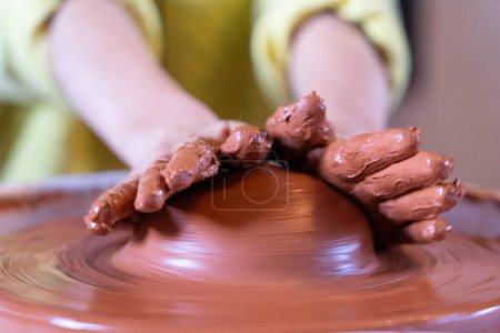 Mains d'enfant tachées d'argile moulant de la poterie sur une roue vue de près