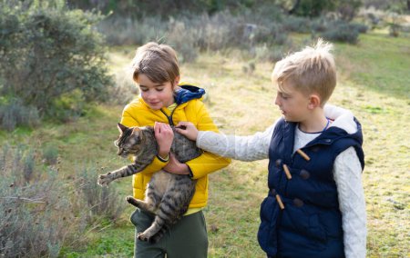 Téléchargez les photos : Deux enfants prennent soin de leur chat à l'extérieur - en image libre de droit