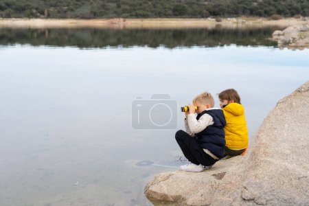 Dos niños observando la naturaleza con prismáticos en un lago