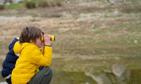 Niño en la naturaleza mirando a través de binoculares con un abrigo amarillo