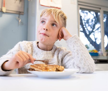 Junge mit Pfannkuchen zum Frühstück in der Küche seines Hauses