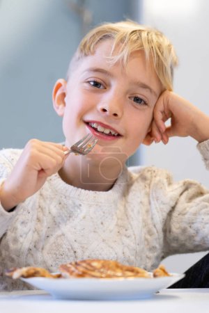 Lächelnder Junge schaut in die Kamera, während er Pfannkuchen isst