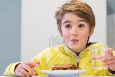Glückliches Kind mit lustigem Gesicht, das Pfannkuchen isst