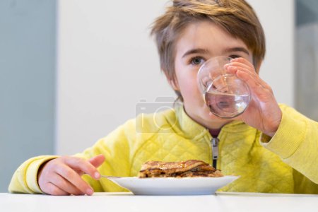 Junge trinkt Wasser und isst Pfannkuchen zu Hause