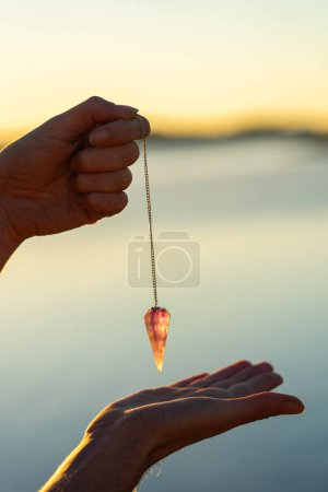 Woman's hands holding a pendulum with a lake behind