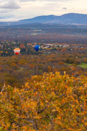 Hot air balloons flying over an autumn landscape