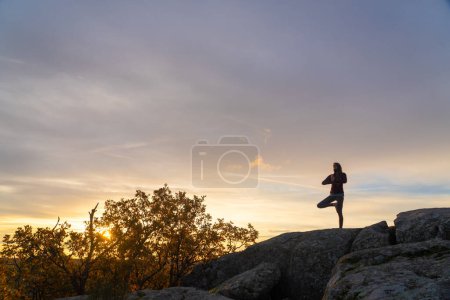 Woman doing yoga tree pose on top of a mountain at sunrise