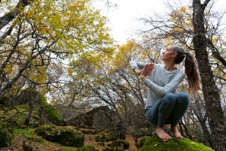 Frau beim Yoga in der Natur, umgeben von Bäumen