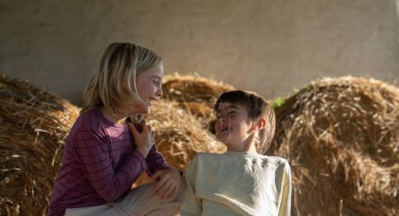 Two children looking at each other smiling on a farm with hay