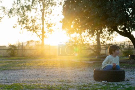 Garçon assis sur un pneu dans le champ au coucher du soleil