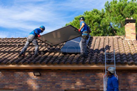 Foto de Tres trabajadores instalando paneles solares en un techo. Energía renovable - Imagen libre de derechos
