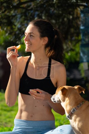 Woman eating a tangerine outdoors with her dog