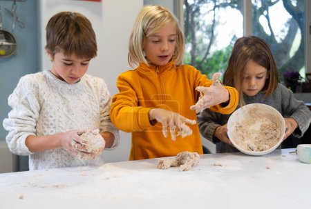 Three children making the dough to make homemade pizza in the kitchen of a house