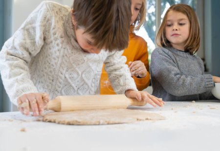 Kinder kochen zu Hause Pizza und machen Teig mit Nudelholz