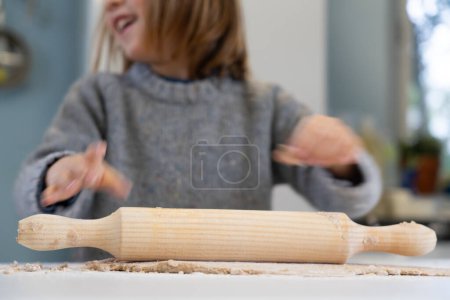 Boy rolling out homemade pizza dough with a rolling pin seen close up