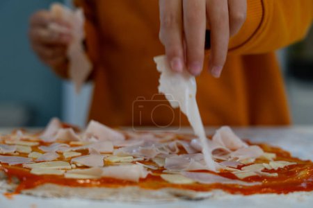 Las manos del niño cocinando pizza casera poniendo los ingredientes en la masa