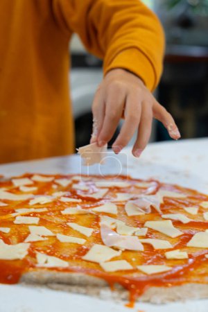 Garçon ajoutant jambon à une pizza maison