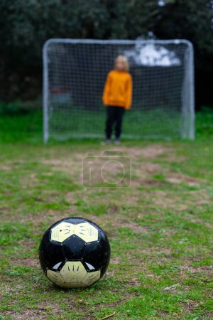 Soccer ball seen up close and a child in a goal in the background