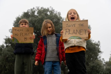 Tres niños protestando contra el cambio climático con letreros de "Salvemos el planeta" y "No hay planeta B"