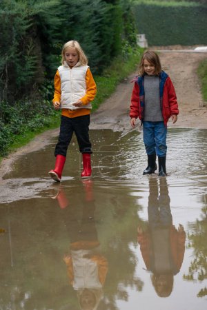Zwei Kinder laufen mit Gummistiefeln durch eine Pfütze