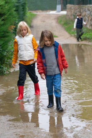 Two children walking over a puddle