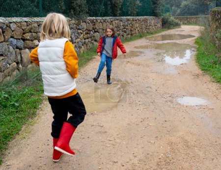 Two children playing splashing in a puddle