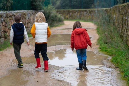 Three children walking along a path with puddles