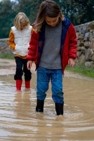 Two children playing in a puddle with wellies