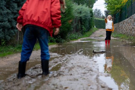 Children playing outdoors in the mud of a puddle