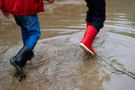 Téléchargez les photos : Children with wellies passing through a puddle with a lot of water - en image libre de droit