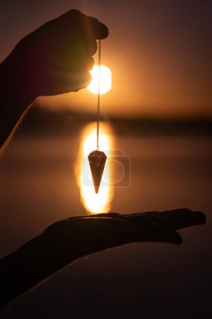 Pendulum seen from up close to against the light at a sunrise on a lake