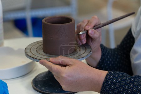 Frauenhände dekorieren ein Stück Keramik in einer Werkstatt