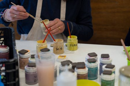 Frau bemalt Keramikstücke in verschiedenen Farben, um eine Glasurfarbenpalette zu erstellen