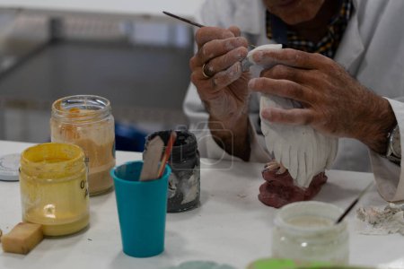 Senior man painting a handmade ceramic figure in a pottery class