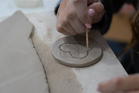 Mains de femme faisant un c?ur avec de l'argile dans un cours de poterie