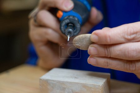 Manos de mujer haciendo manualidades con una piedra con una herramienta rotativa