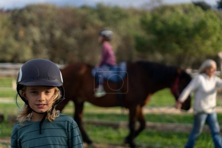 Junge Reiterin mit Reithelm und Kind auf Pferd im Hintergrund