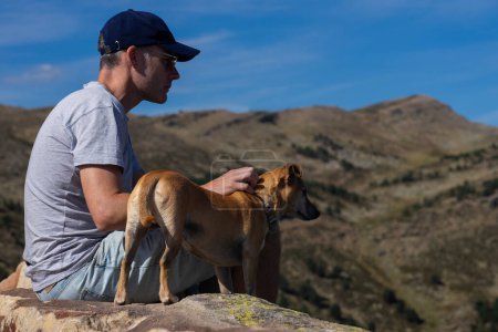 Man with his dog sitting on top of a mountain