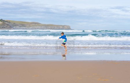 Kind läuft glücklich barfuß an einem jungfräulichen Strand mit Wellen im Hintergrund