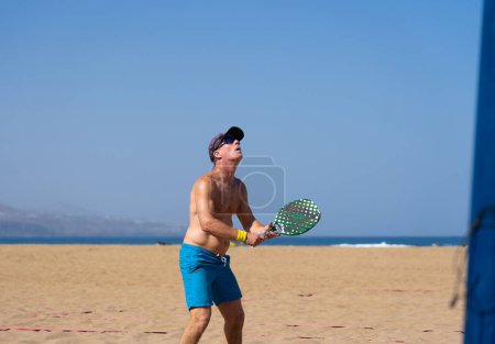 Mature man beach tennis player playing a match