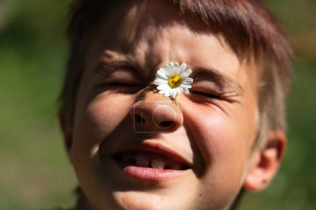 Face of 8 year old caucasian boy happy smiling with a daisy on his face outdoors
