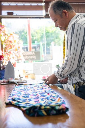 50 year old Latin man fashion designer cutting a fabric in his sewing studio
